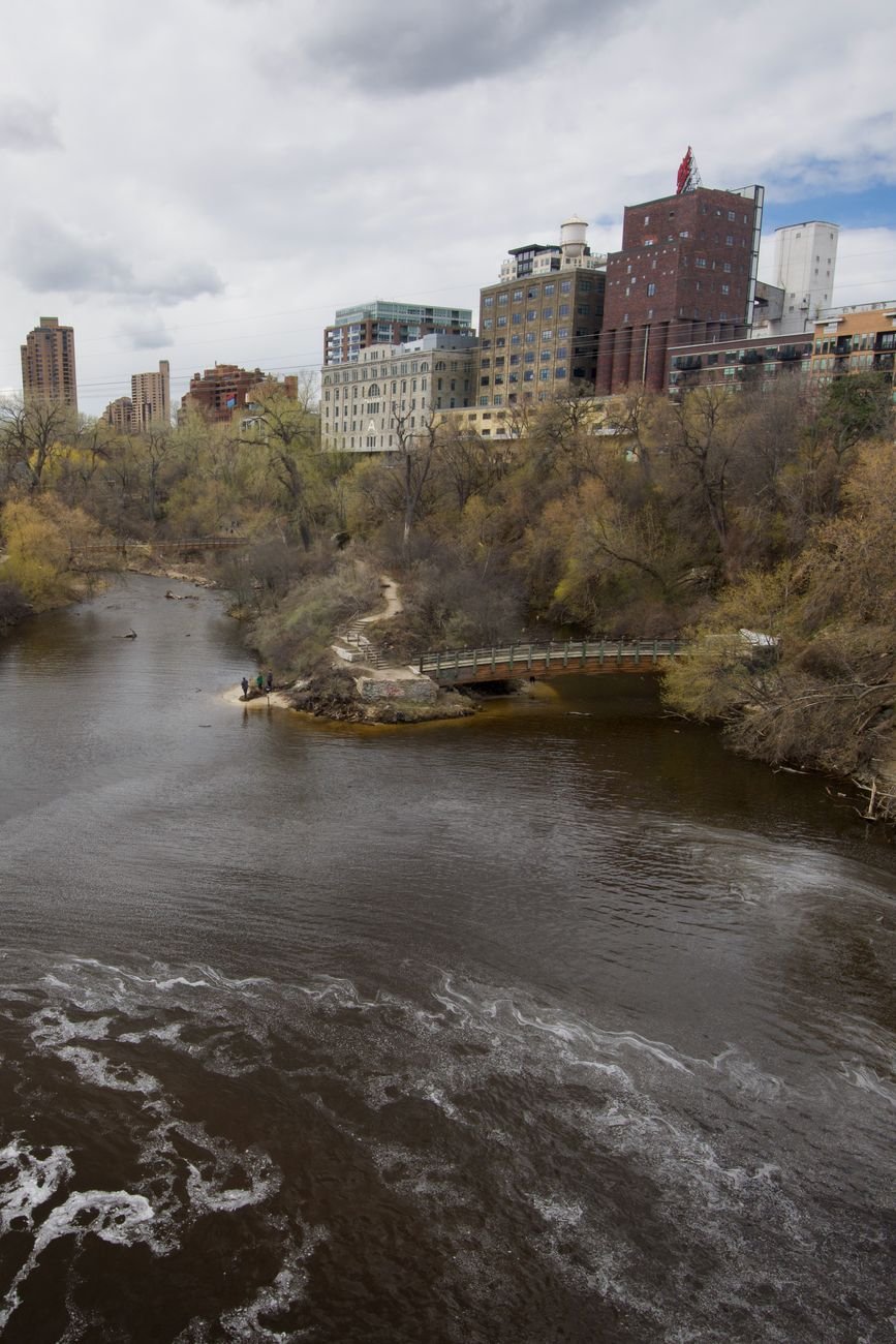 a footbridge and path along the Mississippi River with Minneapolis buildings across the water